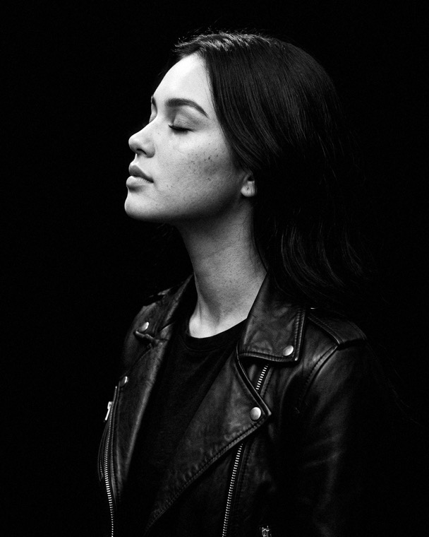 Nova Rai in profile under a single light, eyes closed, black and white